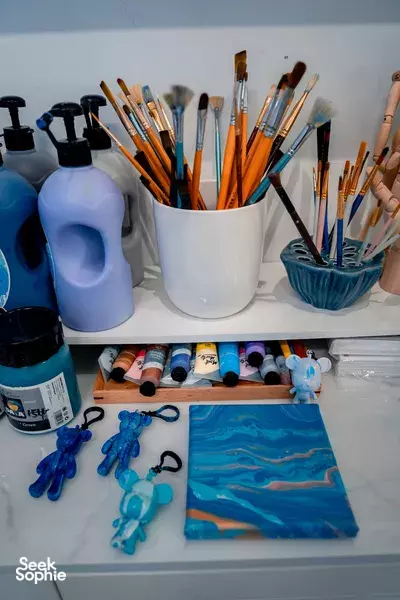 Paintbrushes in cups, acrylic bottles and canvases on a table inside the CocoArt SG art studio for creative workshops in Singapore