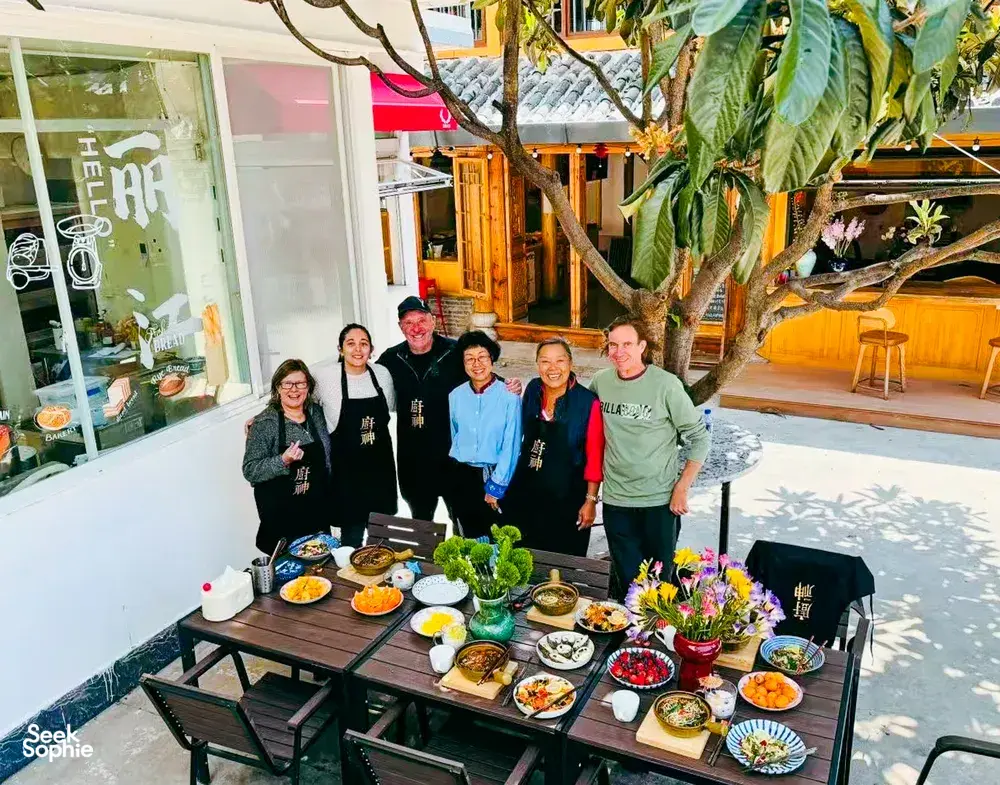 Travellers gathered around a decorated outdoor table of dishes at the end of a Lijiang Yunnan cooking experience in a courtyard
