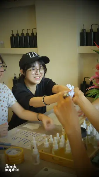 Perfume Play perfume workshop in Singapore: a host helps participants add fragrance drops at a table with small bottles and labelling cards