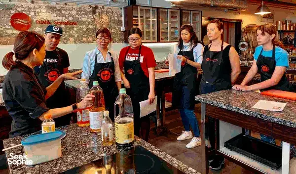 People in aprons prep trays and mix ingredients at a granite counter during a baking charity session in Singapore, workshops in Singapore