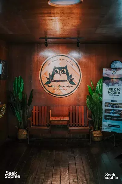 Sukau Greenview Lodge reception wall with owl logo and benches in warm wood, visitor boards on the Kinabatangan River
