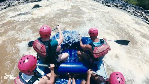 Paddlers seated on a blue inflatable raft with pink helmets navigating foamy rapids on the Padas River during Xtreme Paddlers rafting
