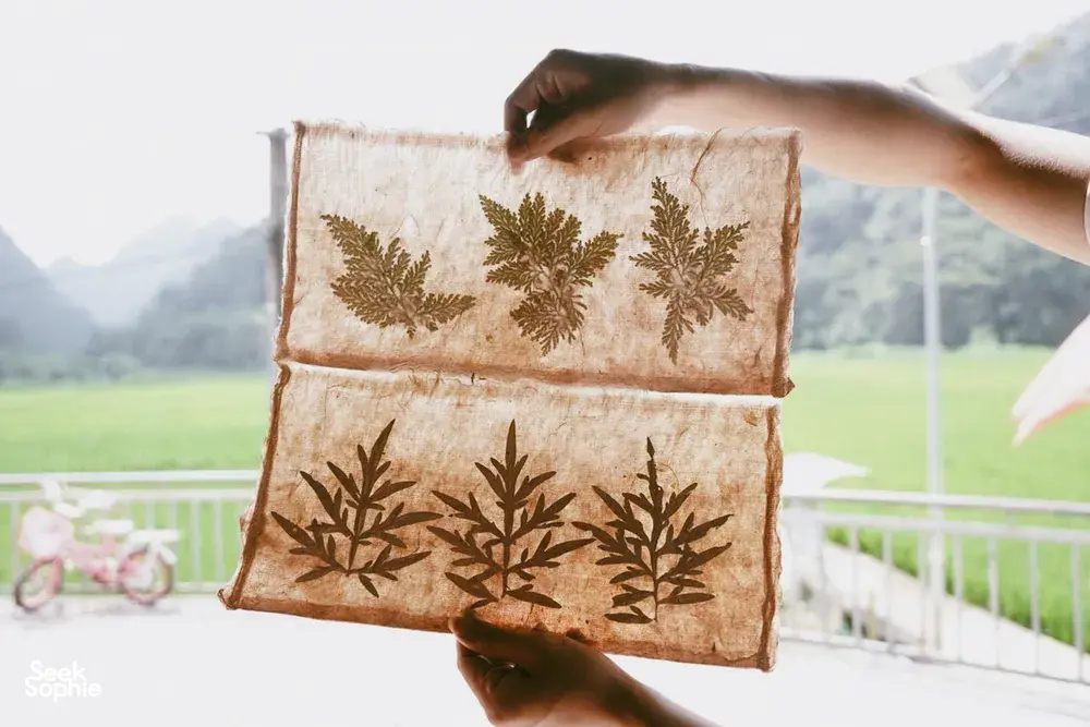 Hands hold a fabric panel with stamped leaf designs at a textile workshop stop on the Cao Bang Loop