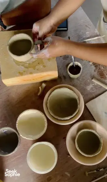 Hands glazing ceramic cups and bowls on a pottery table at Ilham Ceramic Studio in Langkawi’s village workshop