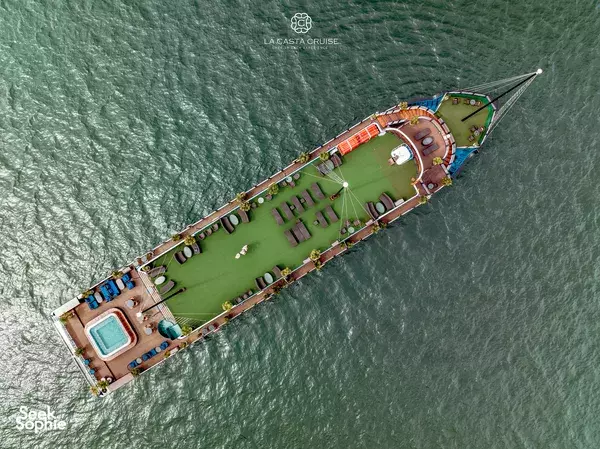 Aerial top-down view of the La Casta cruise with green promenade deck and pool, gliding through Halong Bay waters