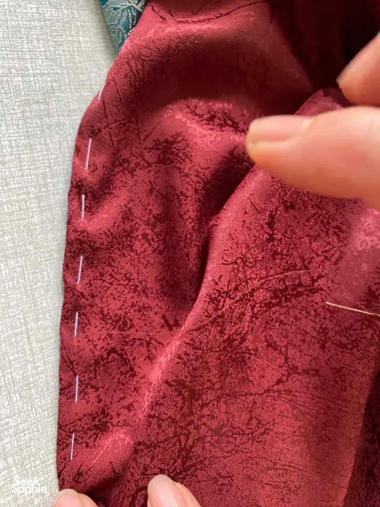 Close-up of hands holding maroon patterned fabric while working on a craft project in a Hanoi Red River village