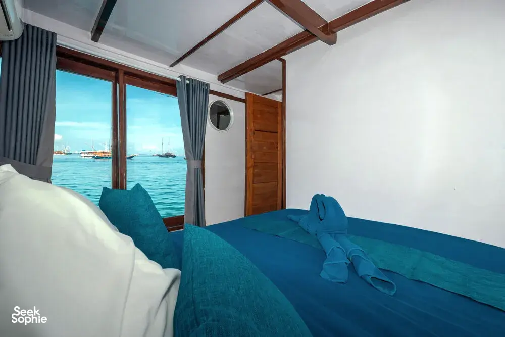 Twin beds in a phinisi cabin with curtains and sea daylight during a private 3D2N Komodo cruise in Labuan Bajo