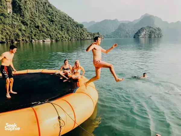 Friends play in the water from an inflatable platform aboard Oasis Bay Party Cruise for a 2D1N party cruise in Halong Bay