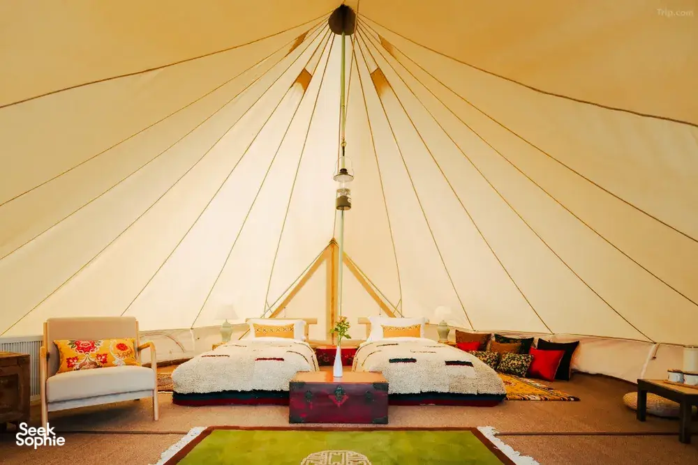 Glamping tent interior at Ferme Liotard in Shangri-La with two covered beds, central rug and a hanging light under canvas