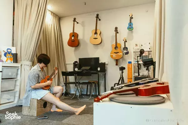 Rehearsal room in Singapore where someone plays an acoustic instrument beside keyboards and wall-mounted guitars — workshops in Singapore