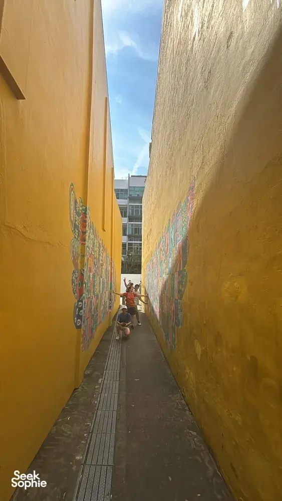 View down a narrow lane between tall yellow mural walls in Katong-Joo Chiat during Monopoly-style team-building in Singapore hidden gems.
