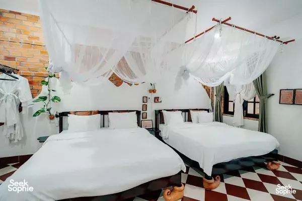 Mekong Delta homestay bedroom with two white beds under draped mosquito nets, set against white walls and checkered floor