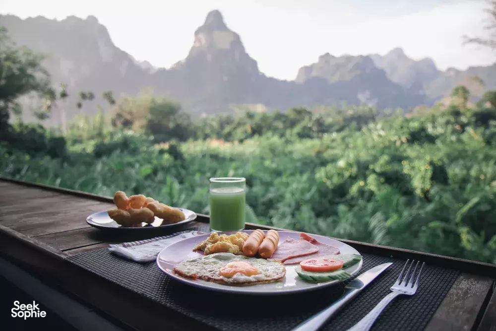 Outdoor breakfast set on a wooden table at Anurak Lodge—eggs, toast and fruit—during a stay in Khao Sok National Park
