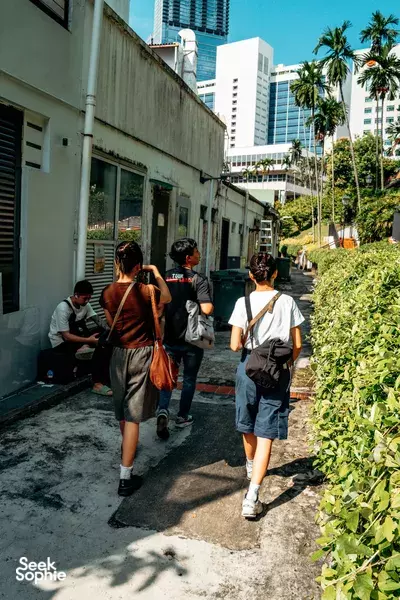 Group of travellers walking down a narrow Singapore lane with greenery and tall buildings during a Triad Trails guided ex-gangster tour