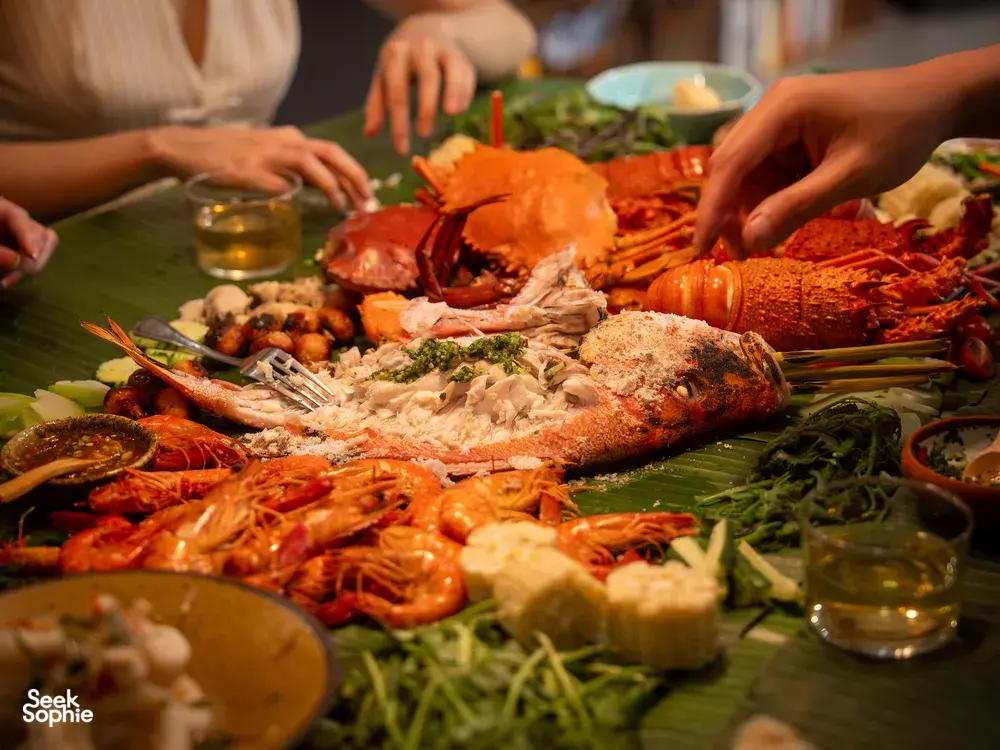 Asian seafood grazing platter with wild greens at Primateve private dining Singapore, with hands serving over a sharing table