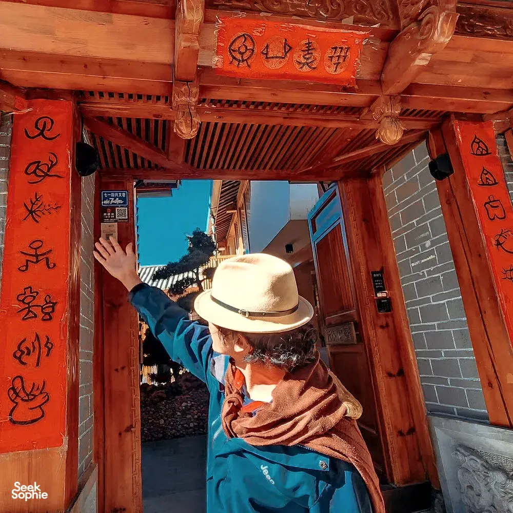 Local guide in a straw hat pointing through a wooden gate in Lijiang’s Old Town, Shuhe Ancient Town with The Bivou Lijiang
