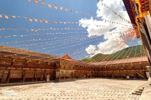 Prayer flags strung over a traditional Tibetan courtyard, with ornate wooden corridors and blue sky at Shangri-La