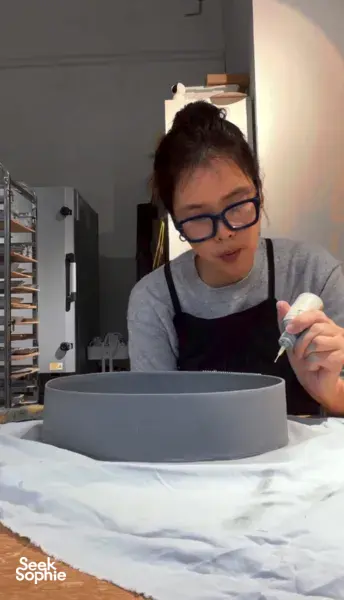 Potter from Ina Atelier shaping a small ceramic bowl over a grey plate on a workshop table during workshops in Singapore