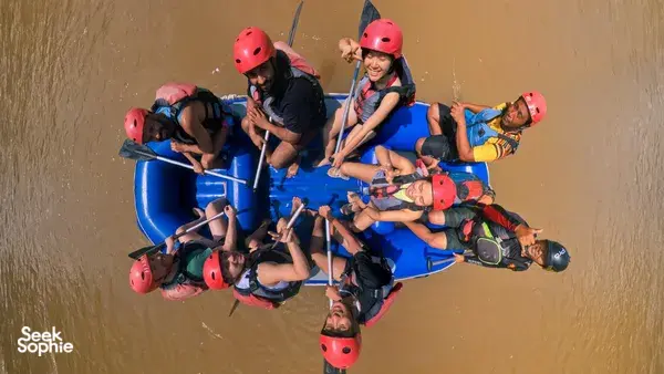 Overhead view of helmeted rafters clustered on a blue inflatable raft on the Padas River in Sabah, with paddles raised over rapids