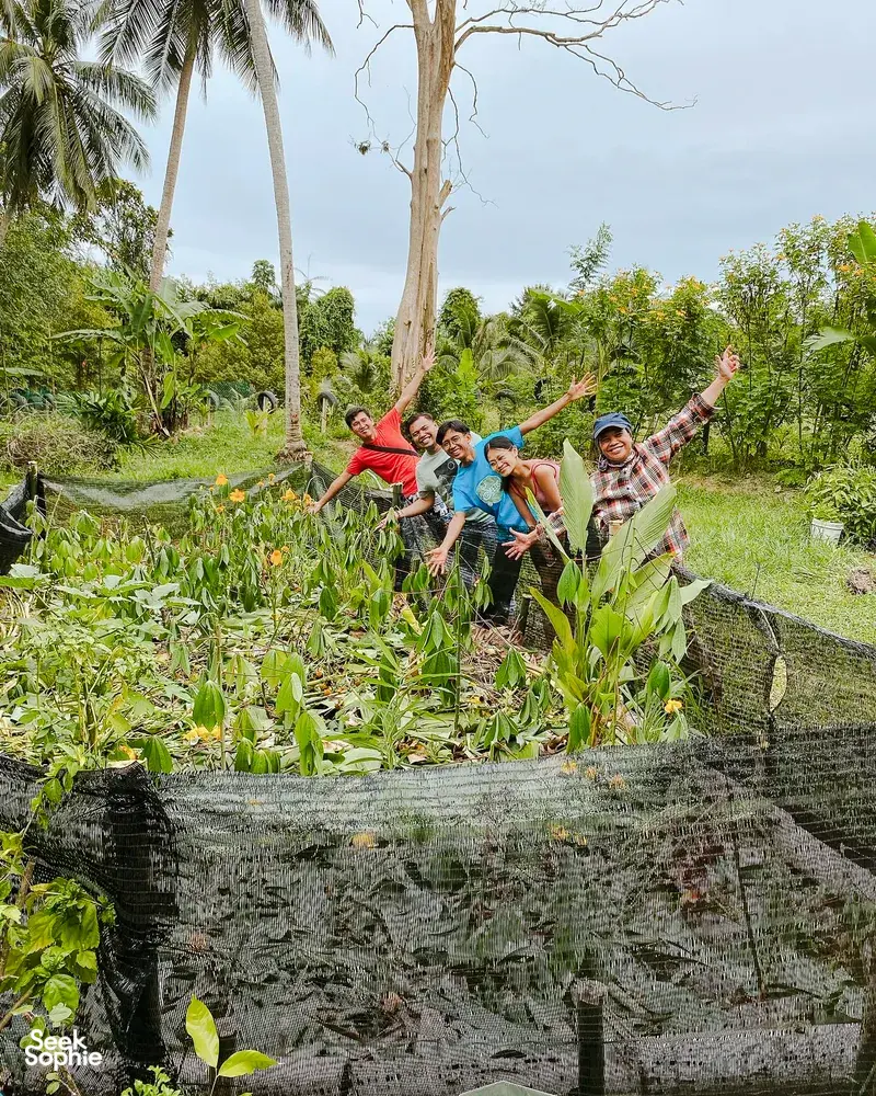 Travellers posing in the greenery of Kebun Lidstari permaculture farmstay, Langkawi, with raised garden beds and palms nearby