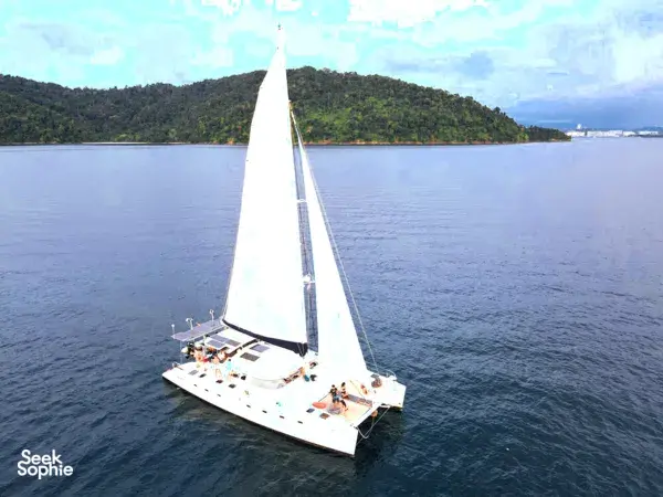 Sailing yacht cutting through calm water with white sails against green hills on a private sunset yacht sail from Kota Kinabalu