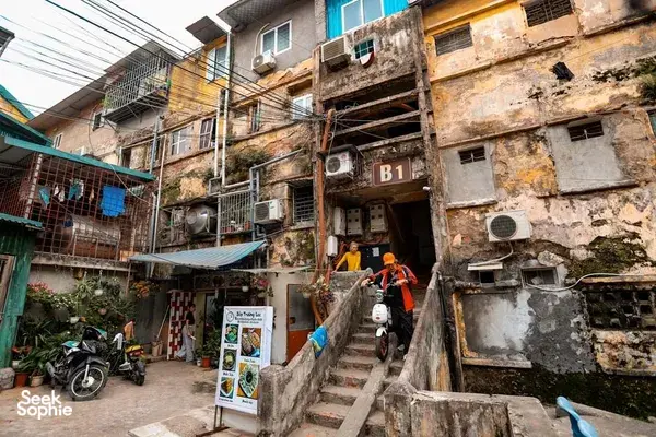 Lorong sempit di kawasan perumahan kolektif di Hanoi, dengan bilik-bilik bertingkat, jeriji tingkap, dan sebuah motosikal di sebelah pintu apartmen bernombor "31"