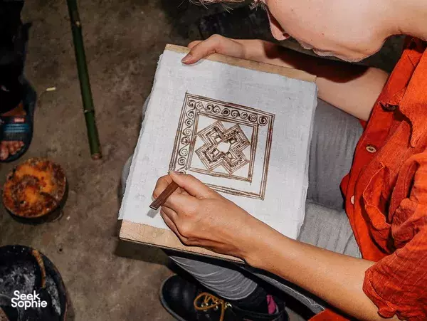 Close-up of hands completing a gold-patterned square on fabric with a tool in a Vietnam printing craft workshop