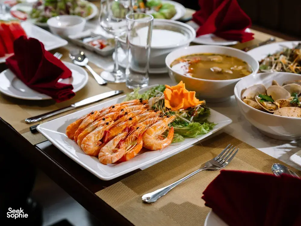 Cat Ba cruise dinner with grilled prawns on a platter, surrounded by bowls of soup and salads on the table