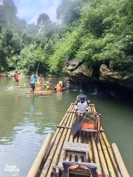 Bamboo raft cruising a calm river through dense rainforest in Khao Sok National Park, with travellers paddling ahead
