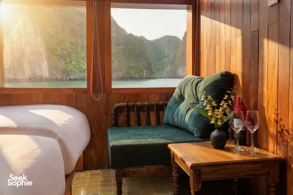 Cosy wooden cabin lounge on Cat Ba Ocean Cruises’ 3D2N Cat Ba boutique cruise, with sofa, wine glasses and sea-view window