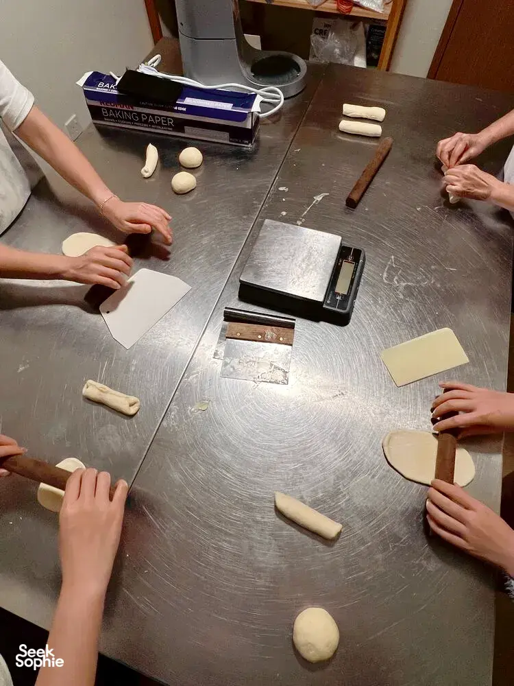 Participants shaping smaller shio pan rolls at The Daily Staples in Singapore, with baking paper, dough pieces and boards laid on the table