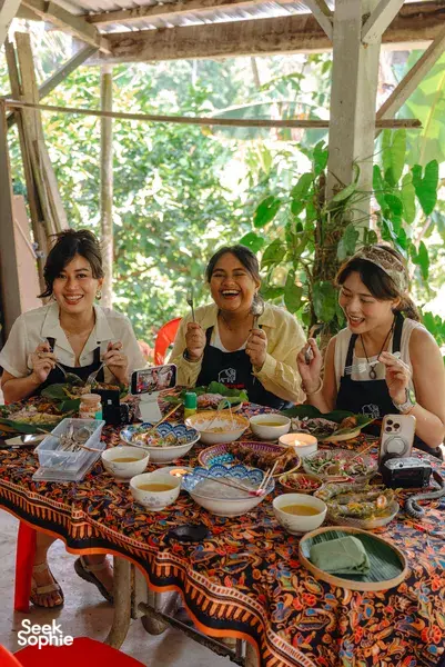 Guests enjoying an Indigenous Sabahan cooking meal in Kota Kinabalu, seated under a wooden shelter with shared dishes
