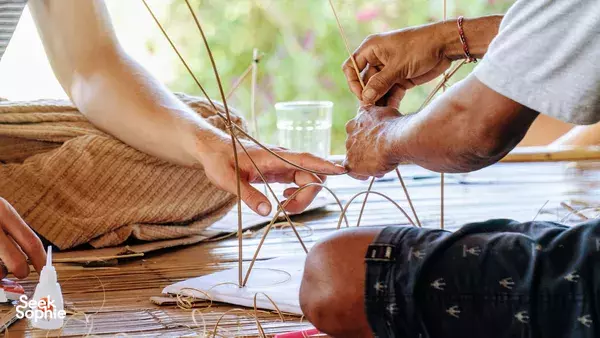 Hands tying bamboo lashings on a woven work mat during a Bamboo Creative Bali bamboo-building design workshop