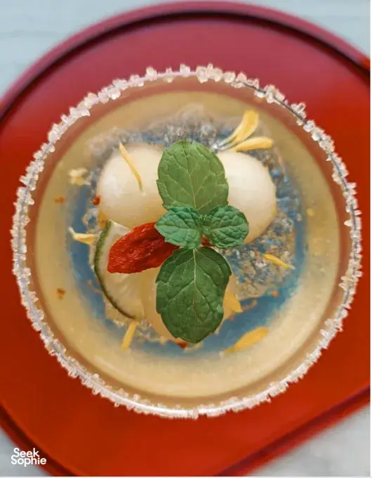 Herbal infusion in a red bowl for TCM mocktails, garnished with mint leaves and sliced roots during workshops in Singapore