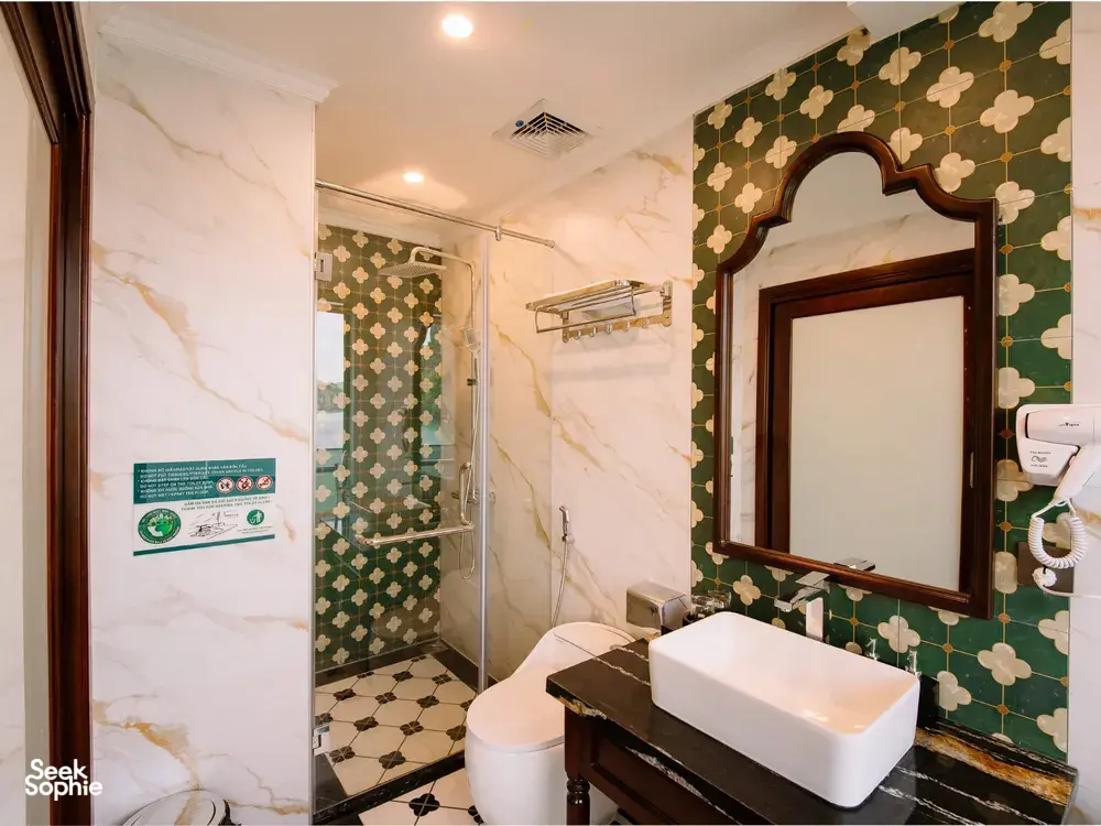 Marble bathroom on a Cat Ba cruise by Sunshine Golden Cruises, with private tub, glass shower and vanity mirror in floral-patterned walls