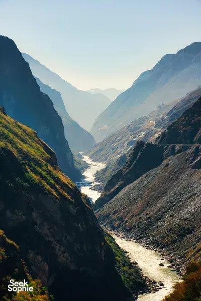 Narrow river gorge flanked by steep mountains in Northern Yunnan, with soft light over a winding valley