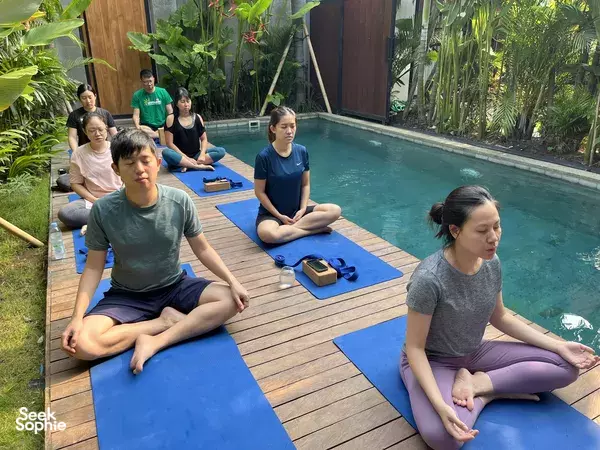Outdoor meditation yoga seated on blue mats beside a Bali villa pool during a private wellness session, Canggu
