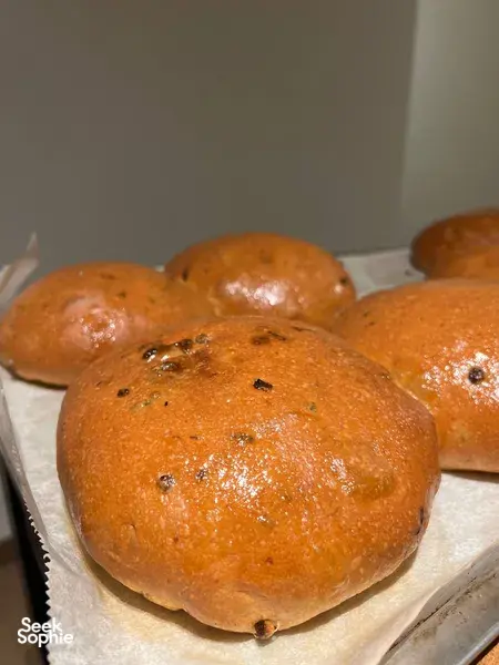 Glazed golden bread rolls with dark herb pieces on parchment at The Daily Staples baking class in Singapore — workshops in Singapore