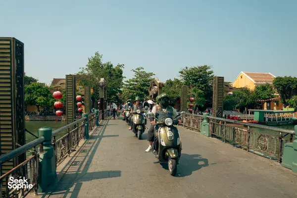 A line of Vespa scooters cruising along a riverside dock in Hoi An with Hoi An Backroad Tours, heading for basket boat fun