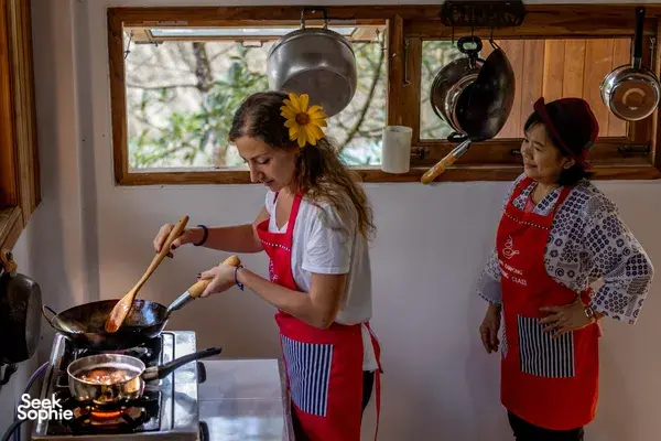 Host-led forage-to-table cooking class in Mae Kampong, Chiang Mai: cook stirs a pan while another instructor watches in a kitchen