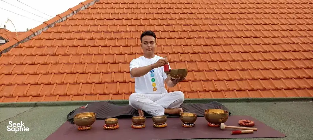 Rooftop sound-healing session in Canggu as ADDA Yoga host sits cross-legged with singing bowls against a tiled roof