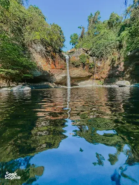 Wide view of a waterfall dropping into a calm pool surrounded by trees in Khao Yai National Park outdoors