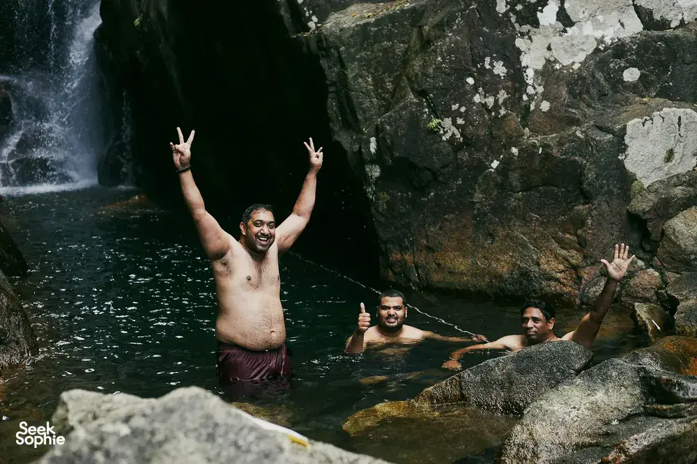 Smiling swimmers pose by a rocky pool under the falls on a Hoi An secret waterfall adventure in Vietnam