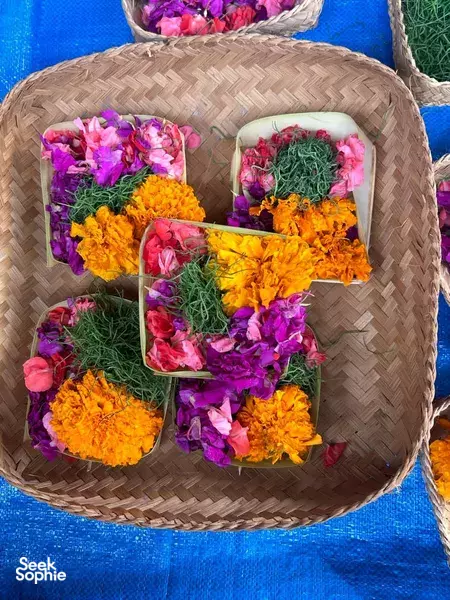Woven basket of bright flower offerings in purple, yellow, and orange for a temple blessing during a Bali ceremony