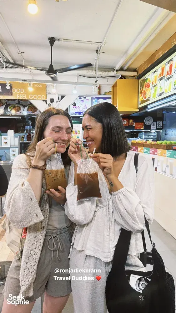 Two travellers smiling and sipping drinks inside an eatery during a private night walk in Geylang, Singapore — Singapore hidden gems