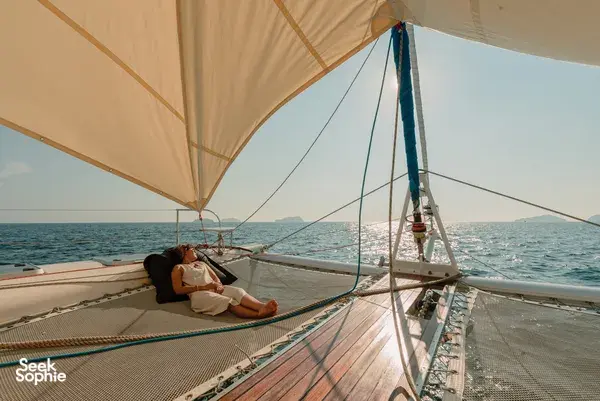 Traveller relaxing on the deck of Mawali catamaran in Kota Kinabalu, Sabah, under sail cover with open sea ahead