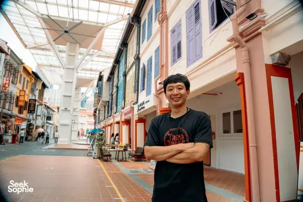 Triad Trails guide standing in a covered Singapore lane beside colourful shophouses during a gritty past walking tour