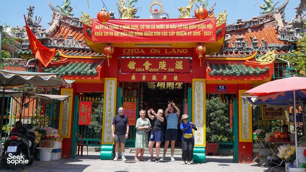 胡志明市一座中式庙宇入口,挂着红色喜庆横幅,庭院里游客挥手拍照