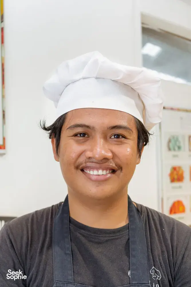 Gili Cooking Classes chef smiling in an indoor kitchen on Lombok during a cooking class, wearing a white hat