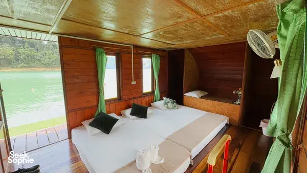 Wooden boat cabin on a Khao Sok cruise with a neatly made double bed, pillows and window curtains — Khao Sok National Park